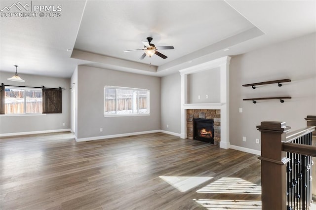 unfurnished living room with a tray ceiling, a stone fireplace, ceiling fan, and a healthy amount of sunlight