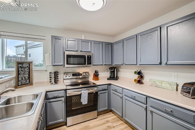 kitchen with appliances with stainless steel finishes, gray cabinets, light hardwood / wood-style floors, and sink