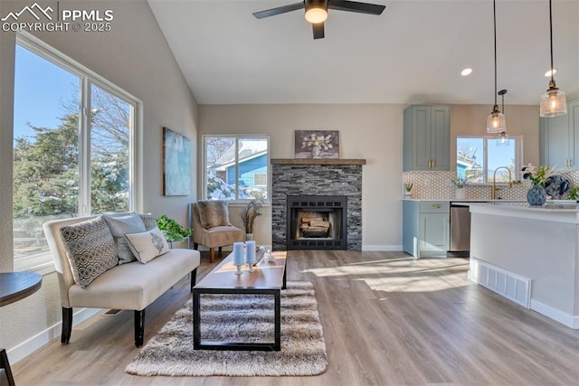 living room featuring vaulted ceiling, light wood-type flooring, ceiling fan, and plenty of natural light