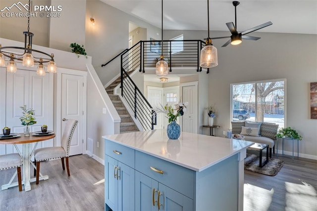 kitchen featuring blue cabinets, decorative light fixtures, a towering ceiling, light wood-type flooring, and ceiling fan with notable chandelier