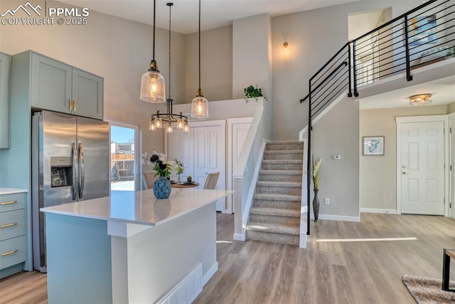 kitchen featuring light hardwood / wood-style flooring, decorative light fixtures, a high ceiling, stainless steel refrigerator with ice dispenser, and a kitchen island