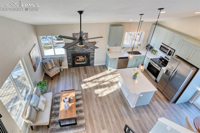 living room with sink, ceiling fan, light wood-type flooring, and a stone fireplace