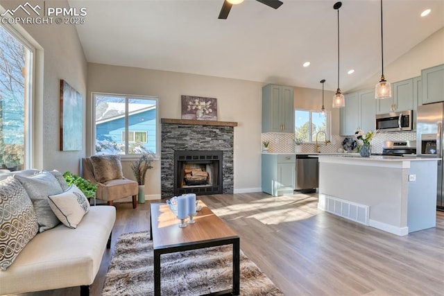 living room featuring a fireplace, ceiling fan, vaulted ceiling, and light hardwood / wood-style flooring