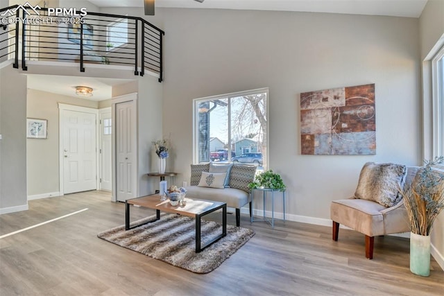 living area with ceiling fan, a towering ceiling, and wood-type flooring