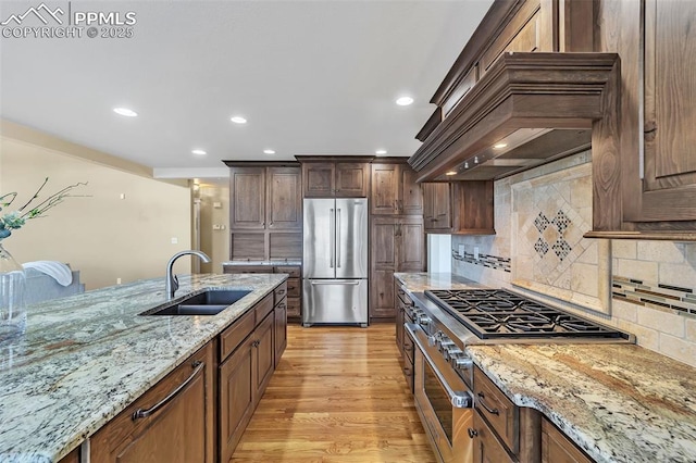 kitchen with sink, stainless steel appliances, light stone counters, light hardwood / wood-style flooring, and decorative backsplash