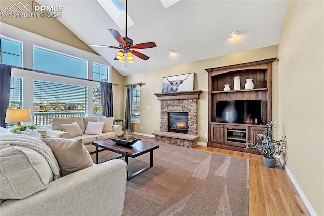 living room featuring a skylight, ceiling fan, built in shelves, light hardwood / wood-style flooring, and a fireplace