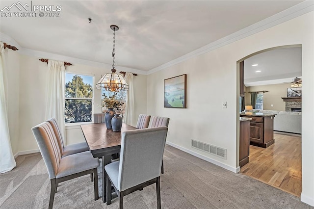 dining space with a fireplace, ceiling fan with notable chandelier, light colored carpet, and ornamental molding