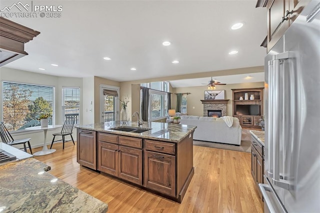 kitchen with a kitchen island with sink, light stone counters, sink, and appliances with stainless steel finishes