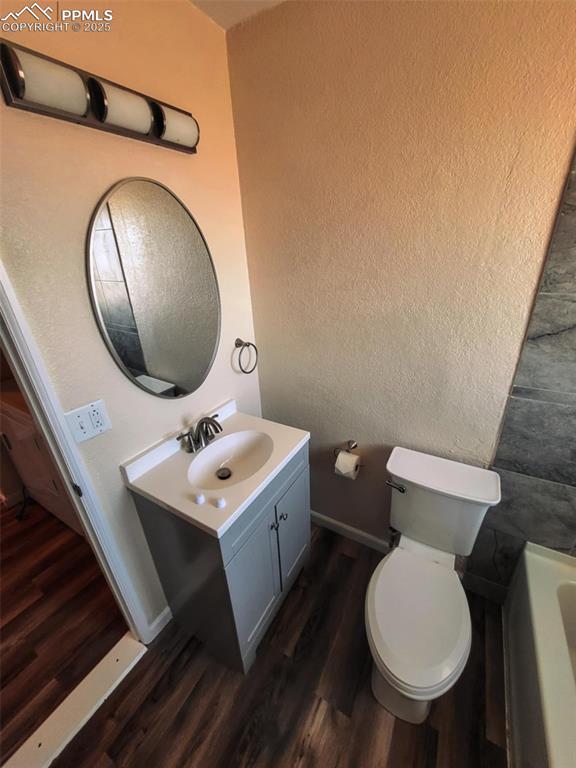 full bath featuring a textured wall, toilet, wood finished floors, vanity, and a bath