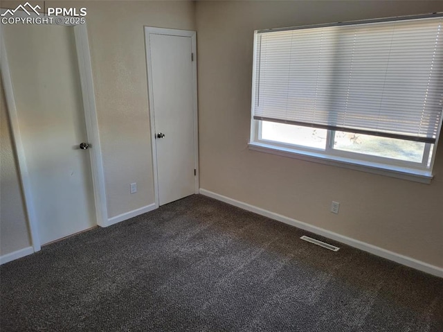 unfurnished bedroom with baseboards, visible vents, and dark carpet