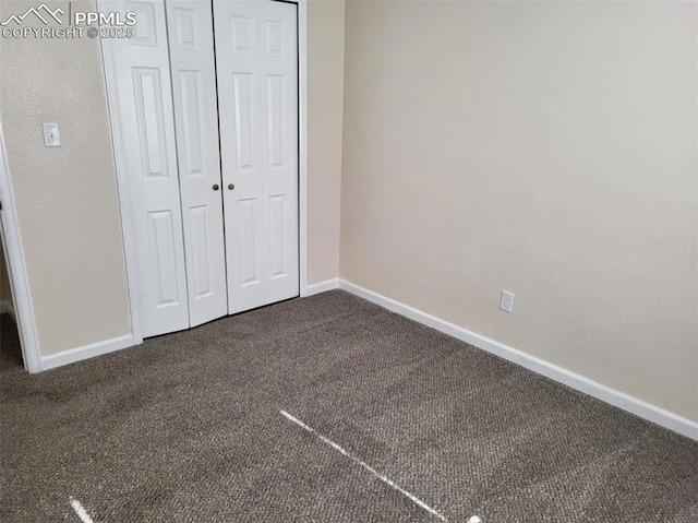 unfurnished bedroom featuring baseboards, dark carpet, and a closet