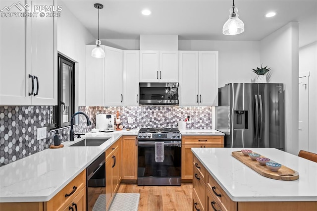 kitchen with white cabinetry, sink, light stone countertops, decorative light fixtures, and appliances with stainless steel finishes