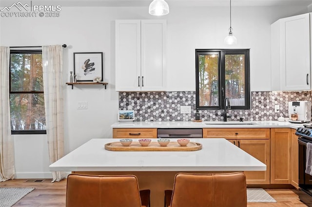 kitchen with a kitchen bar, stainless steel dishwasher, sink, white cabinets, and hanging light fixtures