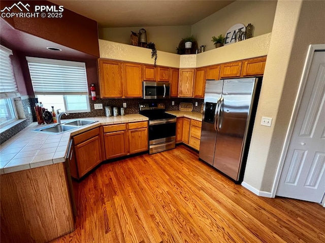 kitchen featuring sink, tile countertops, decorative backsplash, appliances with stainless steel finishes, and light wood-type flooring