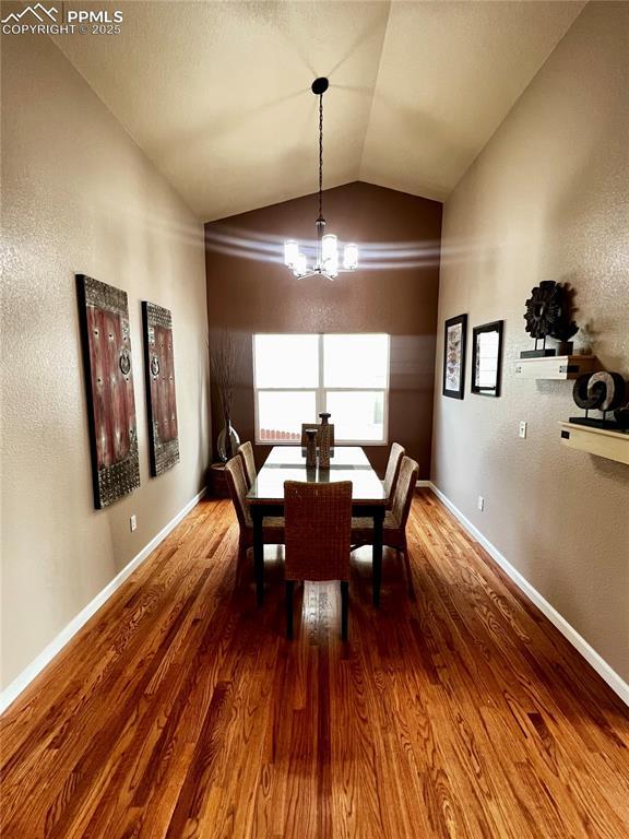 dining area featuring a chandelier, hardwood / wood-style flooring, and vaulted ceiling