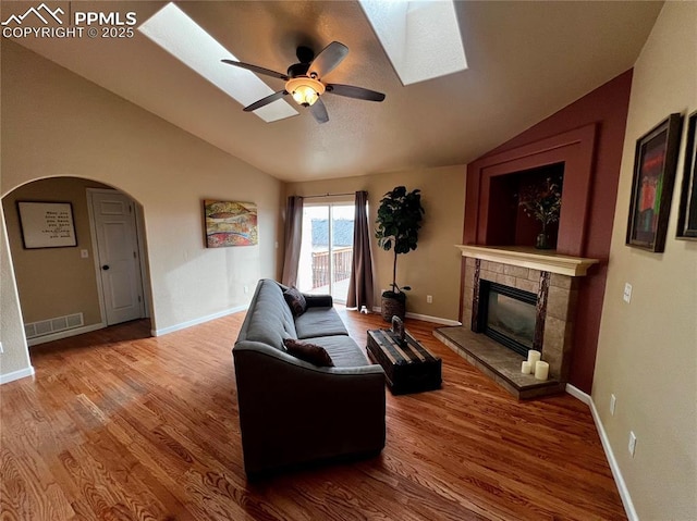 living room featuring ceiling fan, wood-type flooring, lofted ceiling with skylight, and a tile fireplace