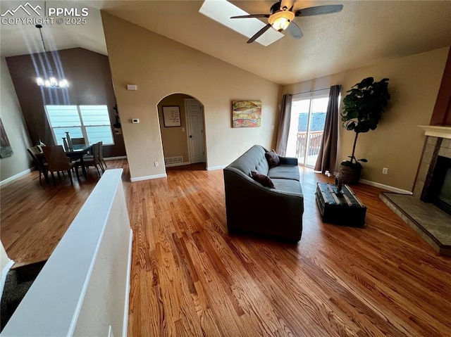 living room with a tiled fireplace, ceiling fan with notable chandelier, wood-type flooring, and lofted ceiling