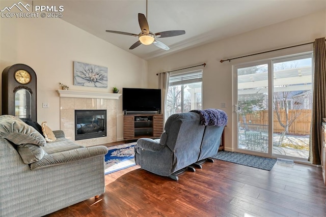 living room featuring ceiling fan, a tile fireplace, vaulted ceiling, and wood-type flooring