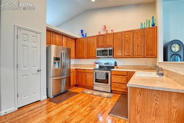 kitchen with vaulted ceiling, appliances with stainless steel finishes, light hardwood / wood-style floors, and sink