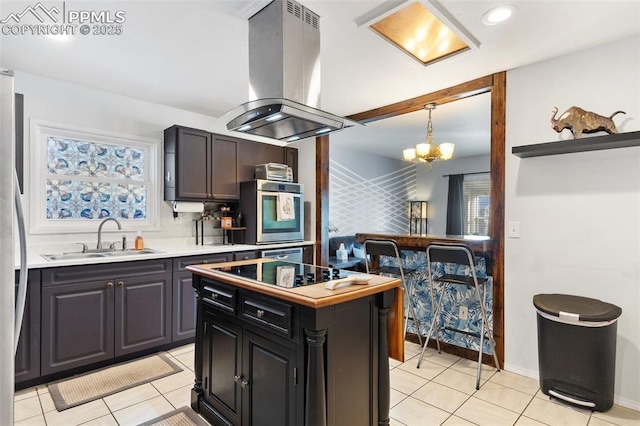 kitchen featuring island range hood, decorative light fixtures, sink, light tile patterned floors, and stainless steel appliances