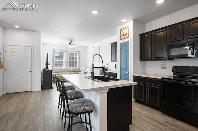 kitchen featuring black appliances, a center island with sink, sink, light wood-type flooring, and a kitchen bar