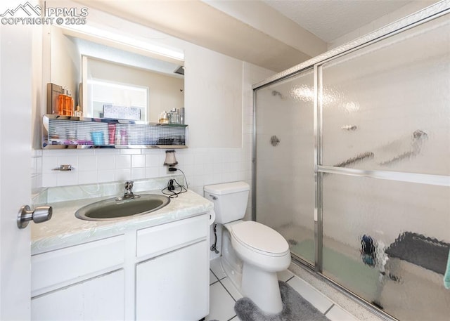 bathroom featuring vanity, toilet, a shower with shower door, and tile walls