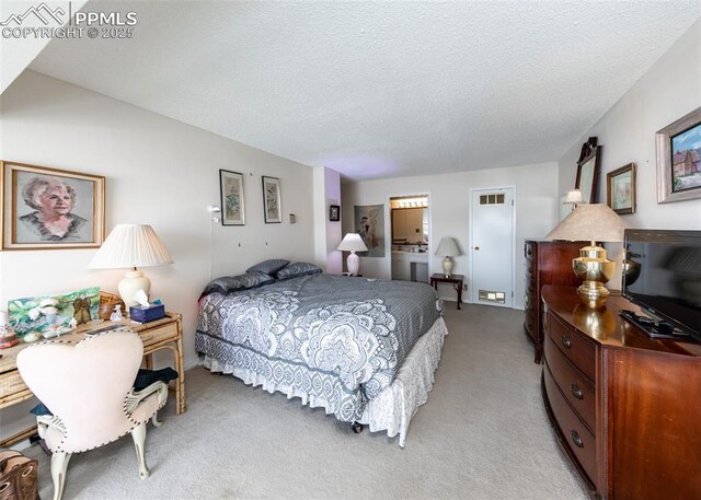 bedroom featuring ensuite bathroom, light carpet, and a textured ceiling