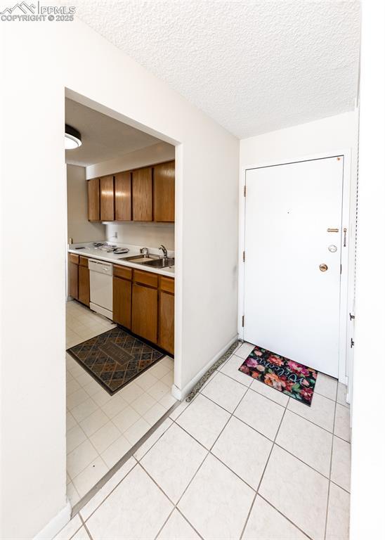 kitchen with white dishwasher, sink, a textured ceiling, and light tile patterned floors