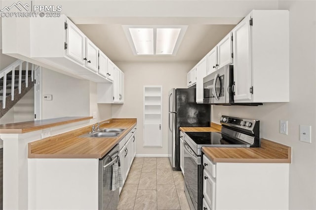 kitchen with kitchen peninsula, appliances with stainless steel finishes, sink, white cabinetry, and light tile patterned flooring