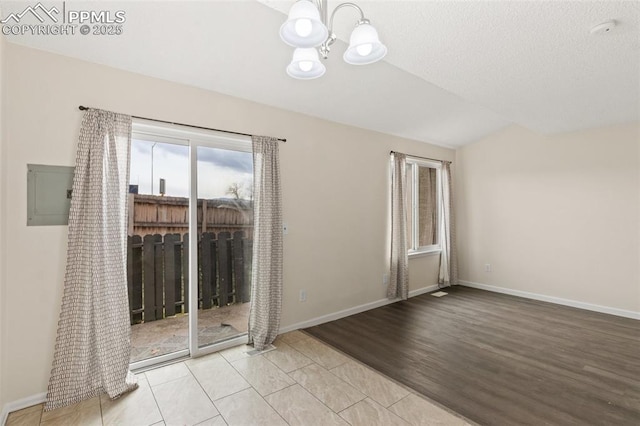 tiled empty room with electric panel, a textured ceiling, and a notable chandelier