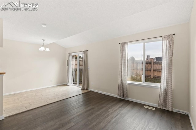 empty room featuring hardwood / wood-style floors, a notable chandelier, and vaulted ceiling