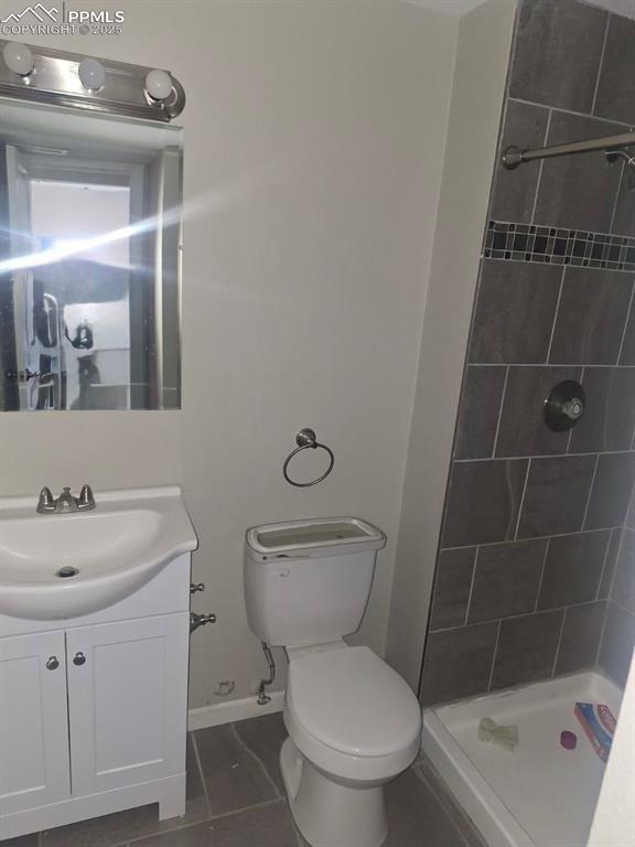 bathroom featuring tile patterned flooring, vanity, toilet, and tiled shower
