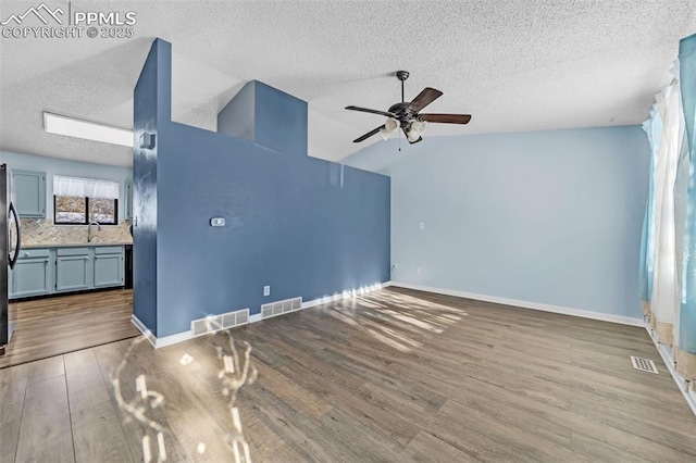 unfurnished living room with hardwood / wood-style flooring, ceiling fan, lofted ceiling, and a textured ceiling