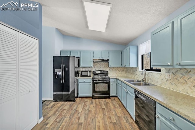 kitchen with sink, light hardwood / wood-style flooring, tasteful backsplash, black appliances, and vaulted ceiling