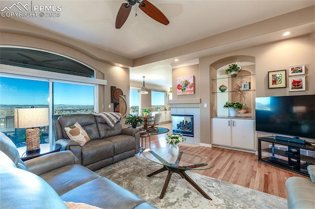 living room featuring a fireplace, built in shelves, light hardwood / wood-style floors, and ceiling fan