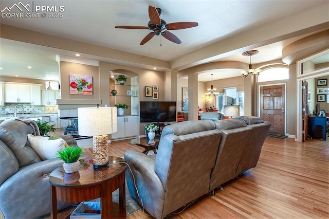 living room featuring sink, light hardwood / wood-style floors, and ceiling fan with notable chandelier