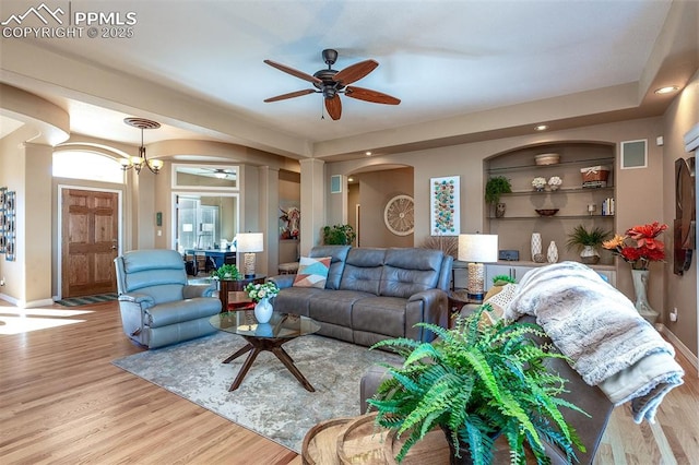 living room with built in shelves, ceiling fan with notable chandelier, and light hardwood / wood-style floors