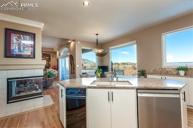 kitchen featuring stainless steel dishwasher, a kitchen island with sink, sink, decorative light fixtures, and white cabinetry