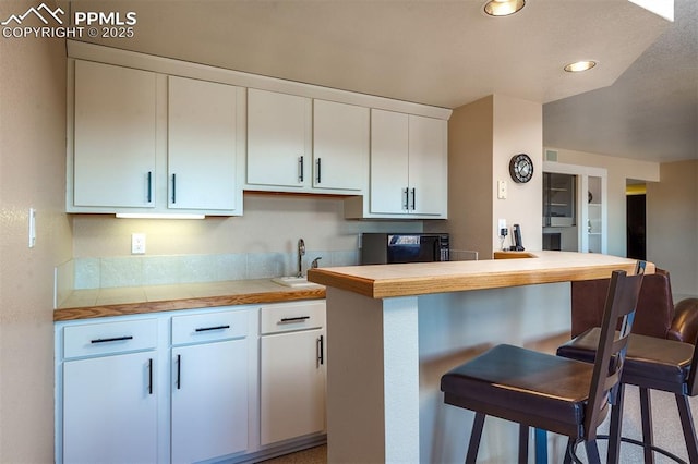 kitchen featuring a kitchen bar, butcher block counters, white cabinetry, and sink