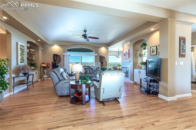 living room featuring built in shelves, light hardwood / wood-style floors, and ceiling fan with notable chandelier