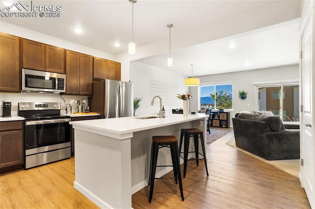 kitchen with a kitchen bar, appliances with stainless steel finishes, a kitchen island with sink, light hardwood / wood-style floors, and hanging light fixtures