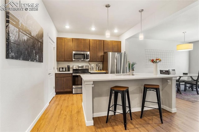 kitchen with a kitchen bar, stainless steel appliances, pendant lighting, a center island with sink, and light hardwood / wood-style floors