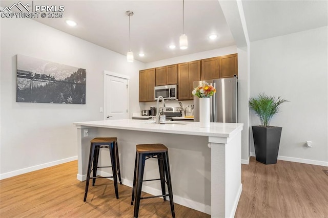 kitchen featuring appliances with stainless steel finishes, light hardwood / wood-style floors, hanging light fixtures, and an island with sink