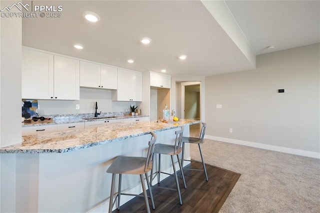 kitchen with a breakfast bar, dark colored carpet, sink, light stone counters, and white cabinetry