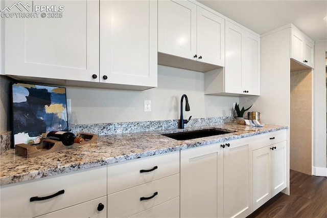 kitchen with white cabinets, light stone counters, dark wood-type flooring, and sink