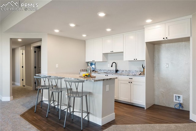 kitchen with dark colored carpet, a kitchen breakfast bar, light stone countertops, a kitchen island, and white cabinetry