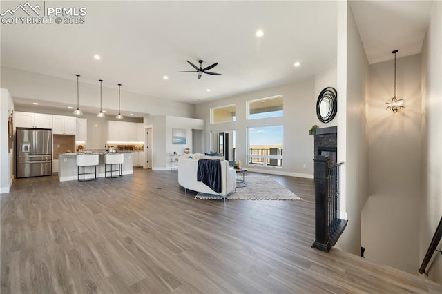 living room featuring hardwood / wood-style floors, a stone fireplace, sink, ceiling fan, and a towering ceiling