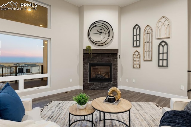 living room with a stone fireplace and dark wood-type flooring