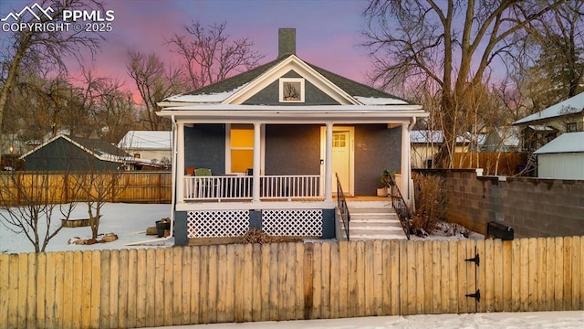 bungalow-style house with a fenced front yard, stucco siding, and a porch