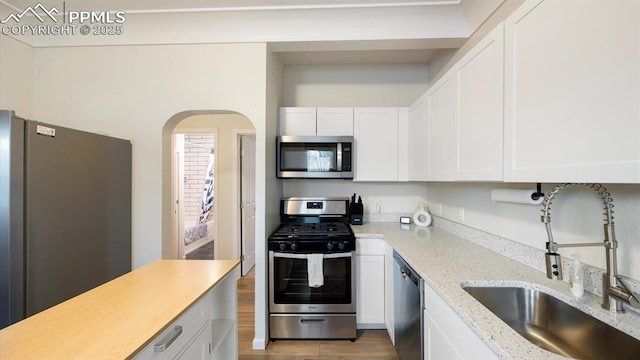 kitchen featuring light stone countertops, stainless steel appliances, wood finished floors, white cabinetry, and a sink